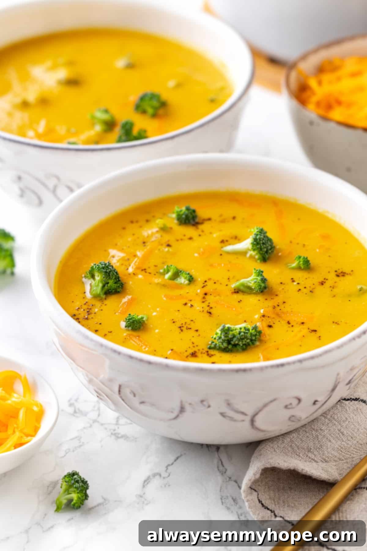 A rich, velvety cheese broth and tender broccoli florets make for a delicious vegan broccoli cheddar soup that's quick and easy to prepare! Two bowls of creamy vegan broccoli cheddar soup, garnished with fresh broccoli florets and vegan cheddar shreds, ready to be enjoyed.