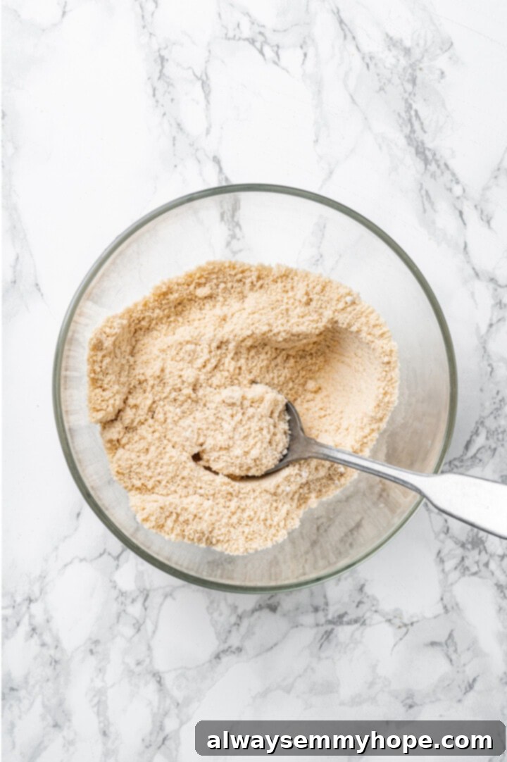 Overhead view of dry ingredients for protein cookie dough in bowl with spoon