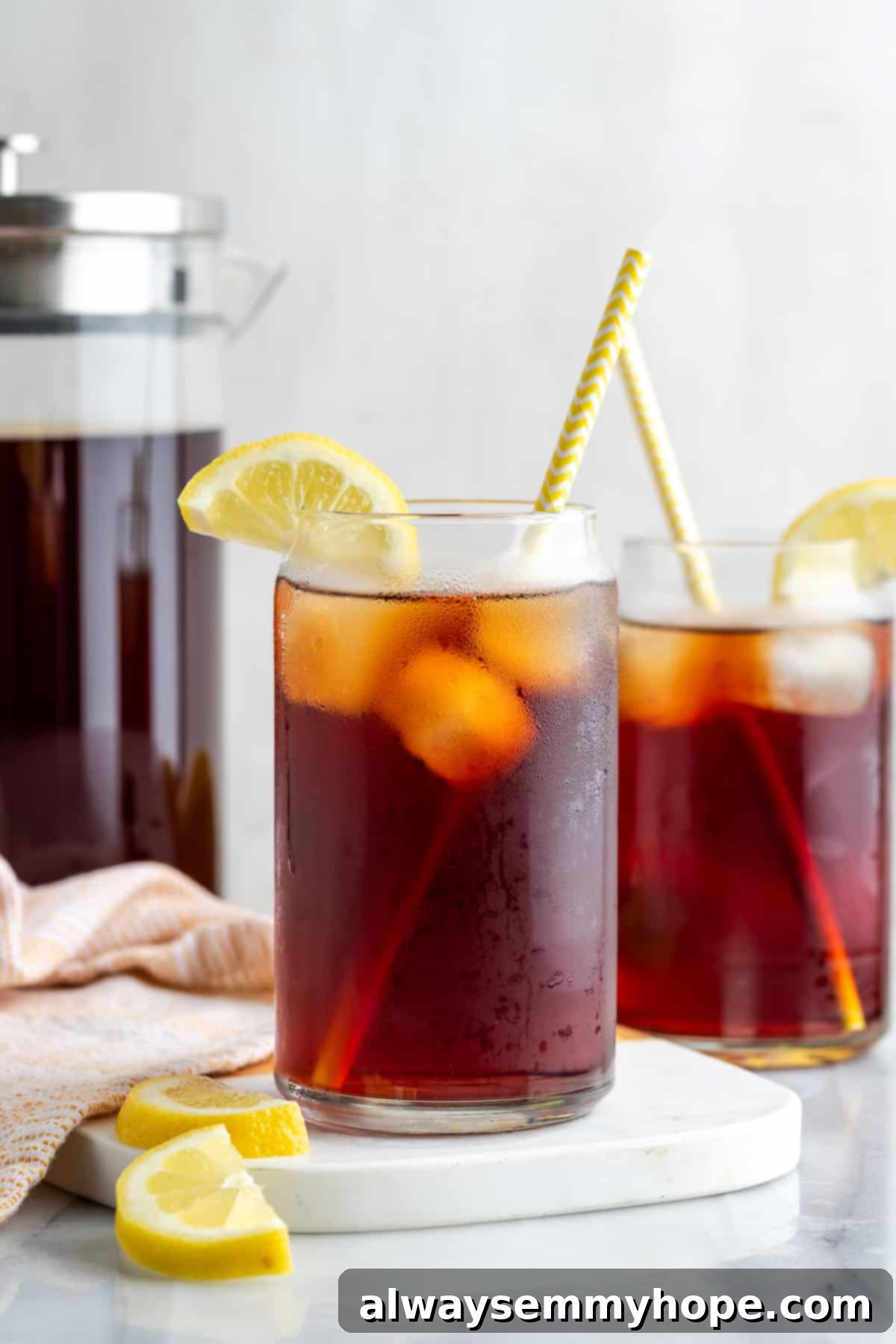 Two glasses of homemade Southern sweet tea with yellow straws and fresh lemon slices, perfectly chilled and ready to enjoy.