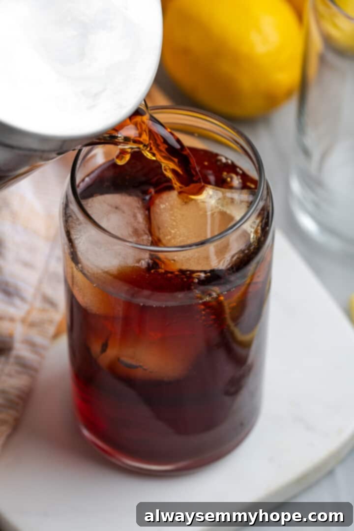 Pouring refreshing Southern sweet tea from a pitcher into a glass filled with ice cubes, ready for serving.