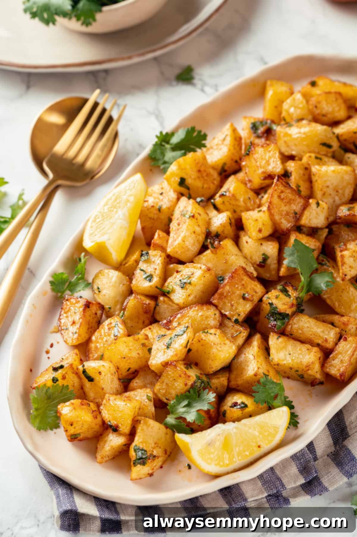 Top-down view of a white platter filled with golden-brown batata harra, garnished with fresh cilantro and lemon wedges.