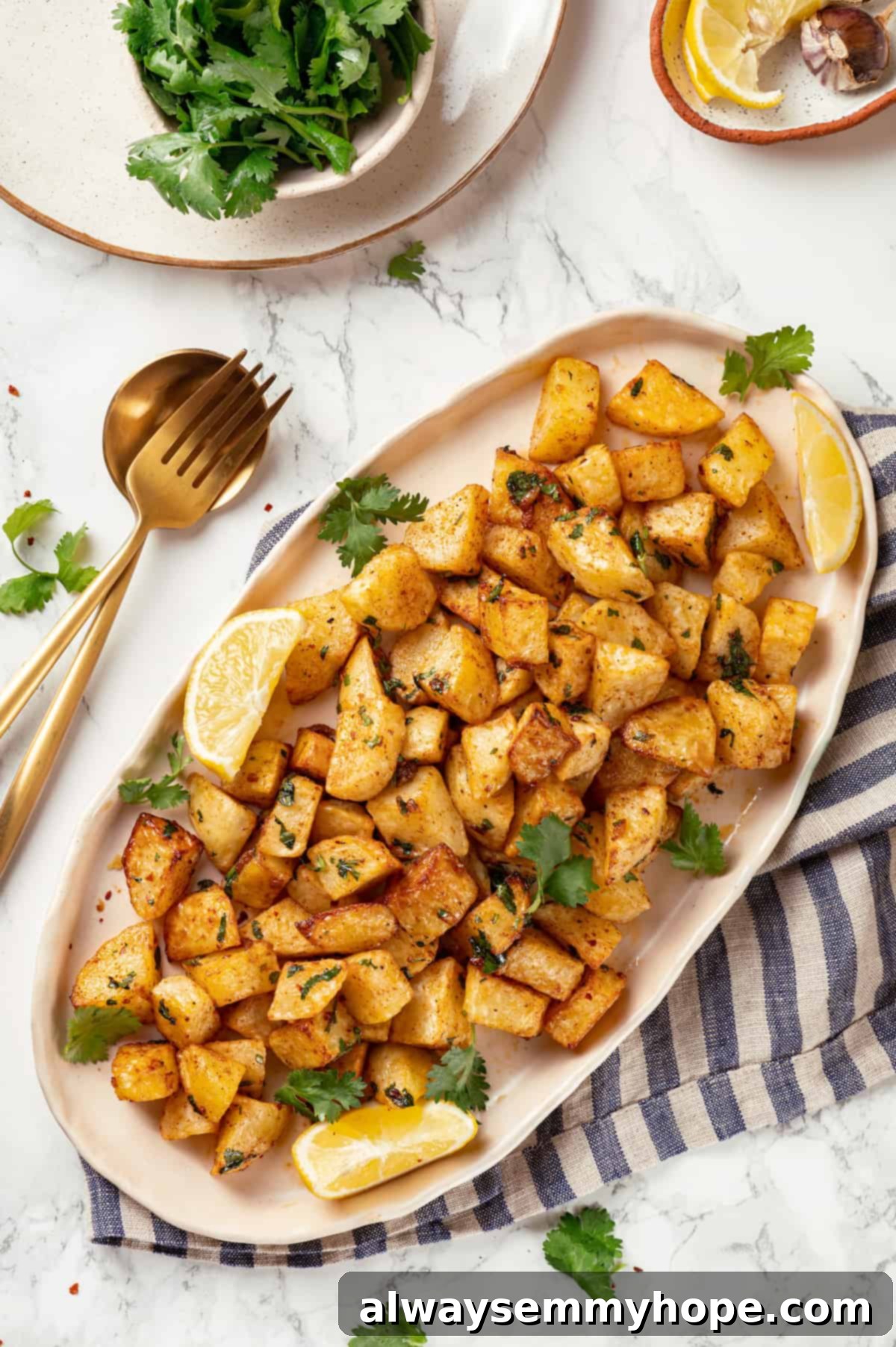 Overhead view of a white platter featuring perfectly cooked Batata Harra, garnished with fresh cilantro leaves and bright lemon wedges.