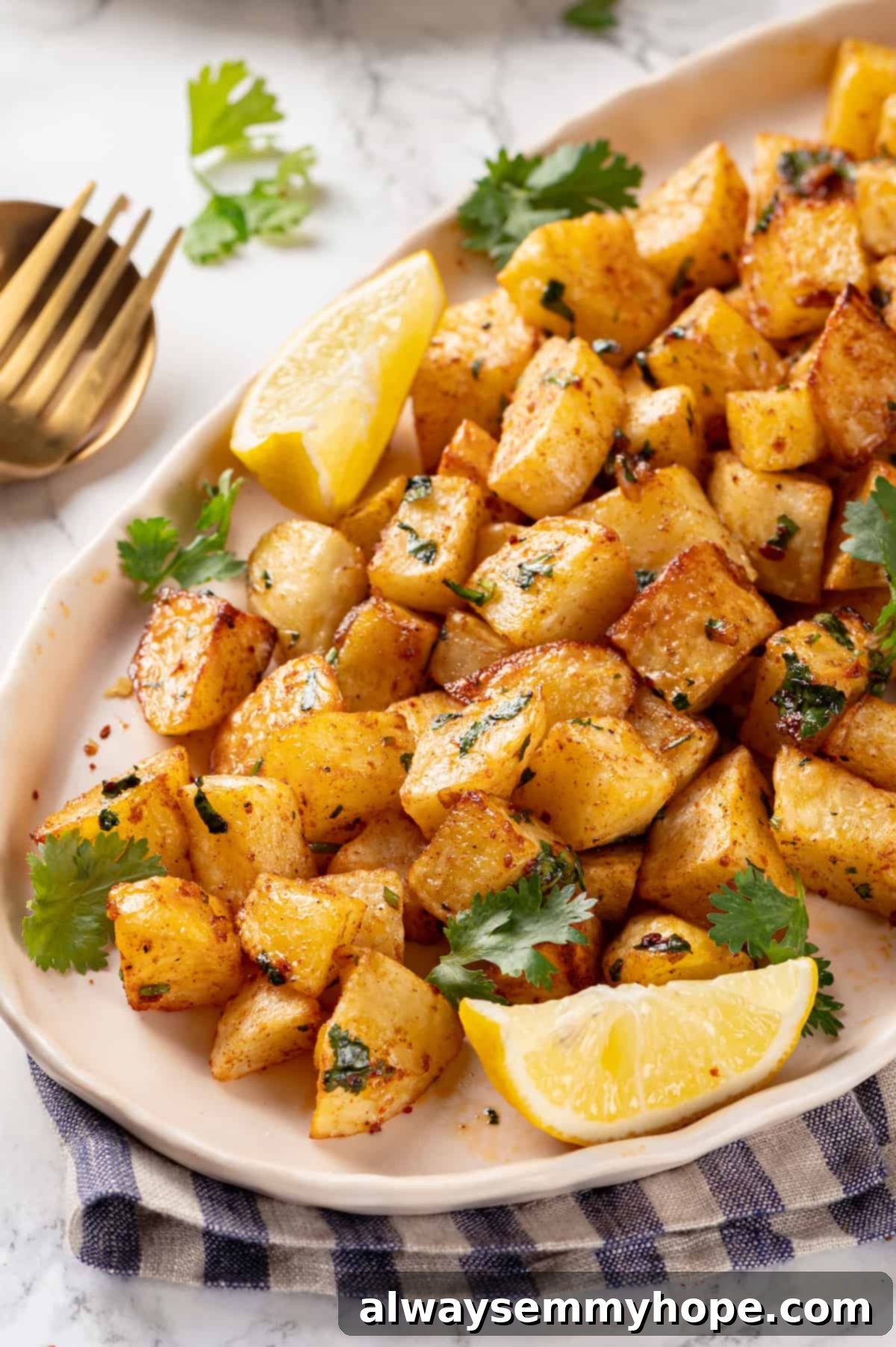 Close-up of crispy Batata Harra on a white platter, showing the vibrant green cilantro and golden-brown potato texture, with lemon wedges.