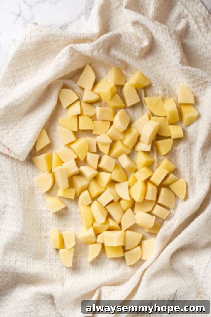 Overhead view of diced potatoes spread on a clean kitchen towel, being patted dry to ensure crispiness.