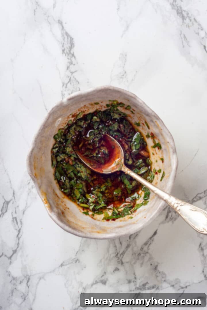 Overhead view of the vibrant green and red spicy sauce for Batata Harra in a small bowl, with fresh cilantro and minced garlic visible.