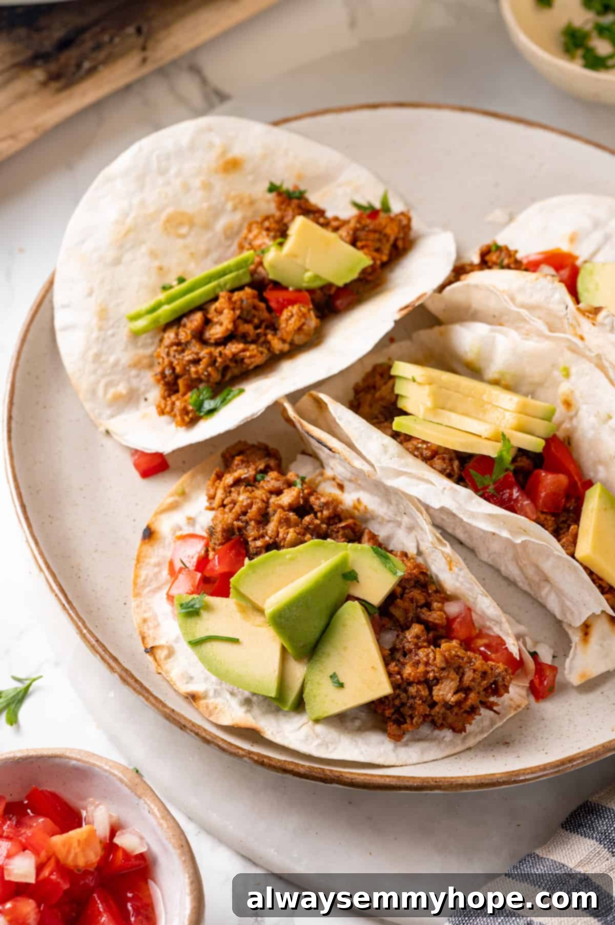 Soyrizo tacos on a plate with fresh avocado slices and diced tomatoes, ready to eat.