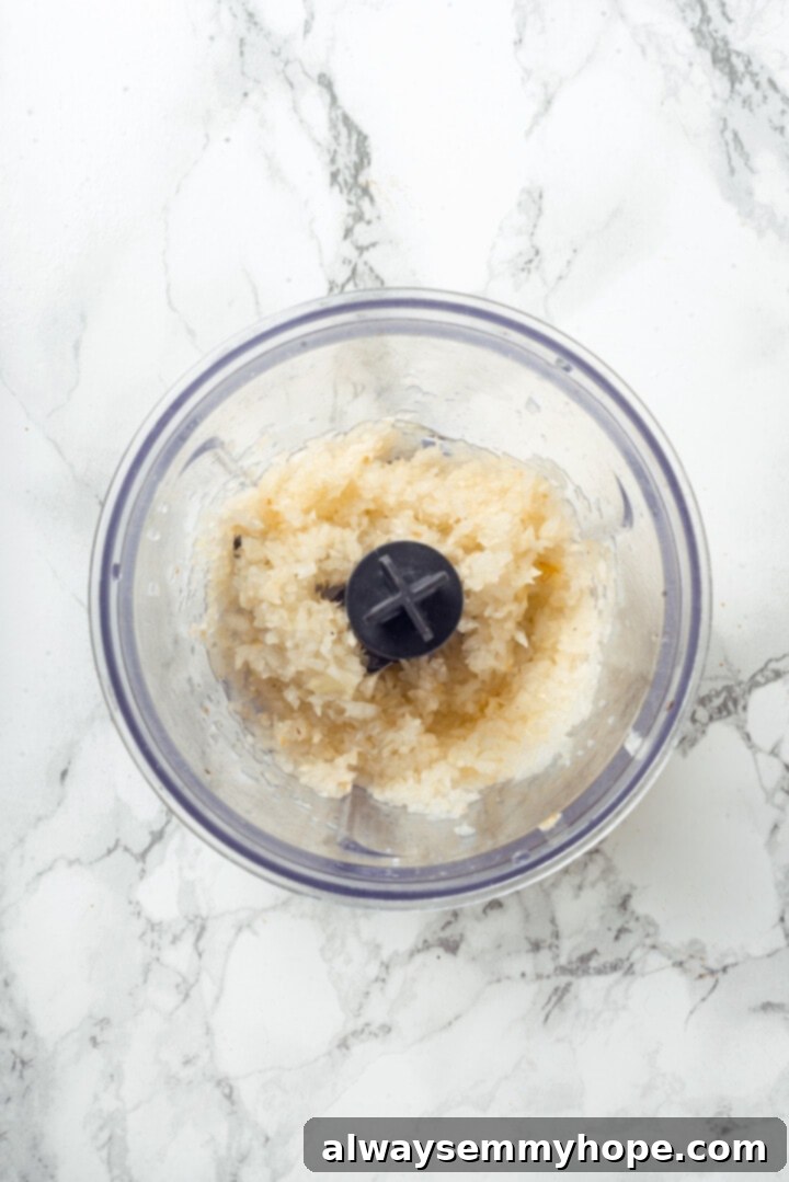 Overhead view of finely minced onions and garlic in a food processor bowl.