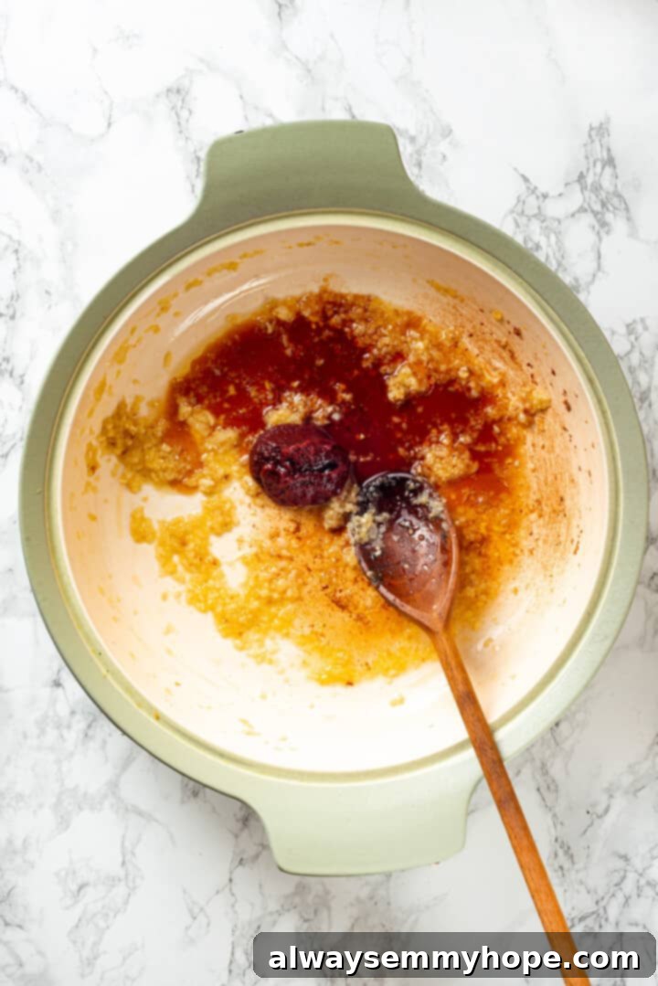 Overhead view of various spices being added to the sautéed onions and garlic in a pan.