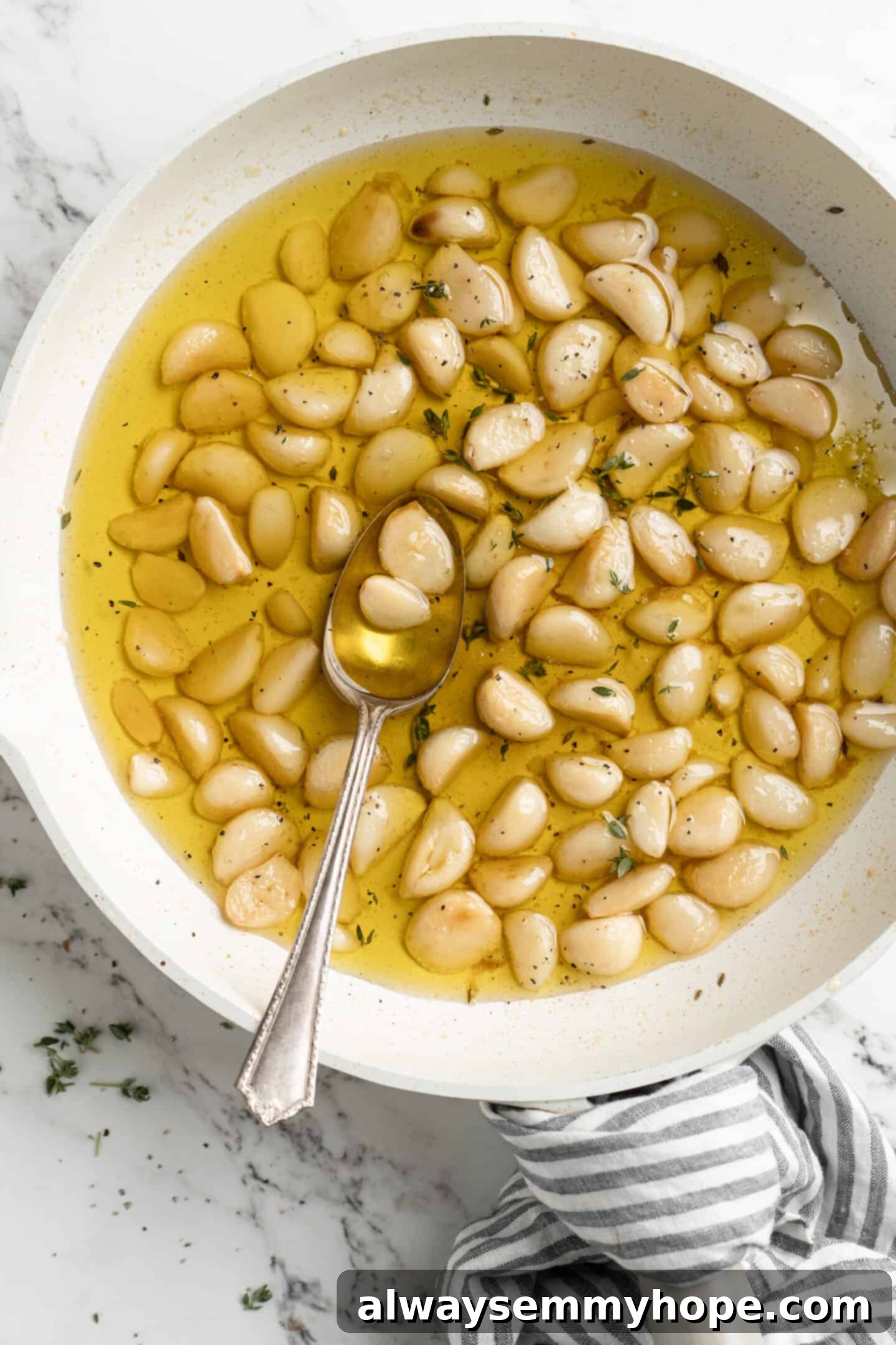 Overhead view of freshly made garlic confit in a pan with a spoon, highlighting the golden color and soft texture of the cloves.
