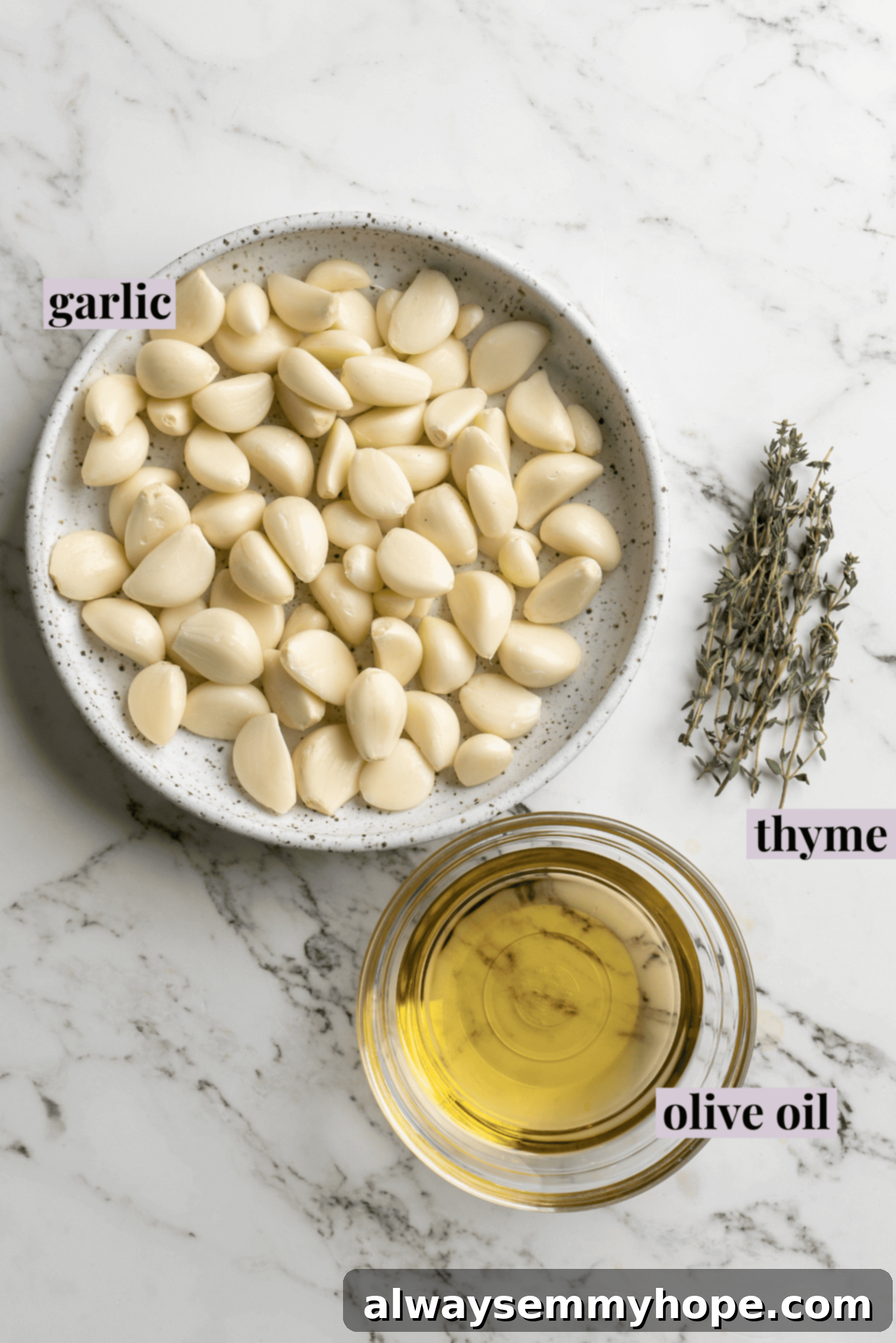 Overhead view of ingredients for garlic confit, including whole garlic heads, fresh rosemary, and a bottle of olive oil, with labels for each item.