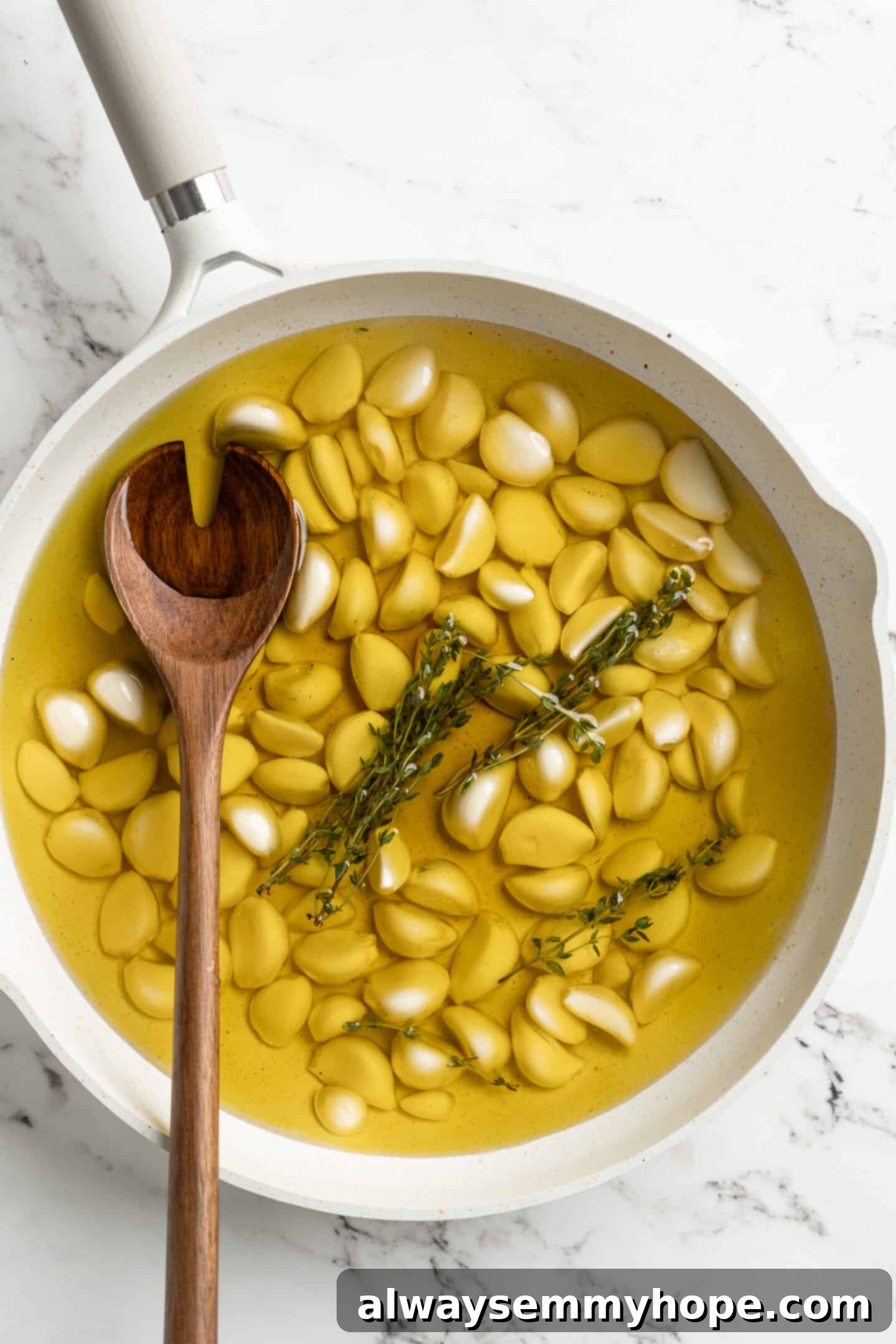Close-up overhead view of peeled garlic cloves, fresh thyme, and olive oil simmering gently in a small pan on the stovetop.