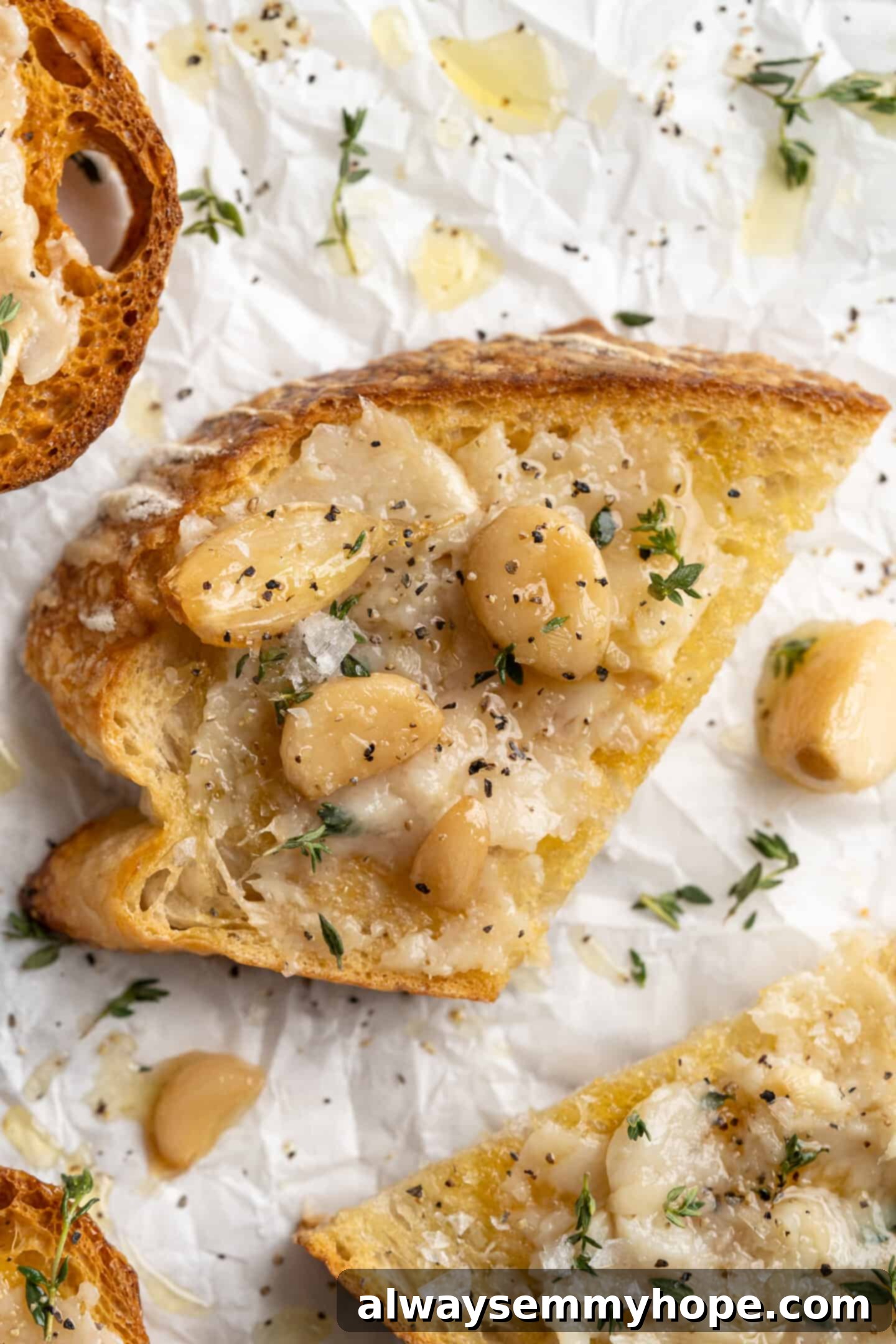 Overhead view of garlic confit spread on sourdough toast, garnished with fresh thyme and freshly cracked black pepper.