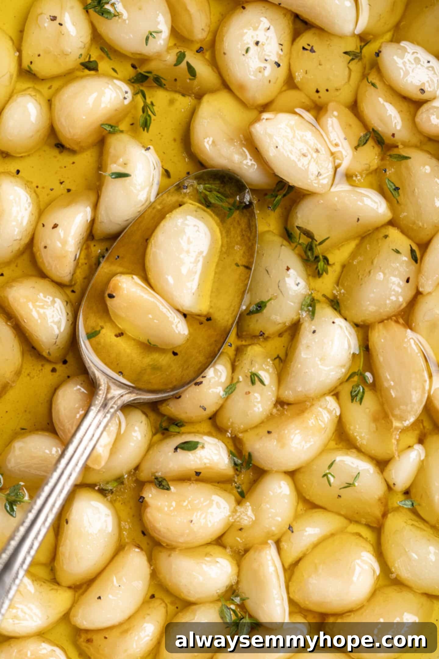 Overhead view of a small spoon resting in a bowl of homemade garlic confit, highlighting the golden color and buttery texture.