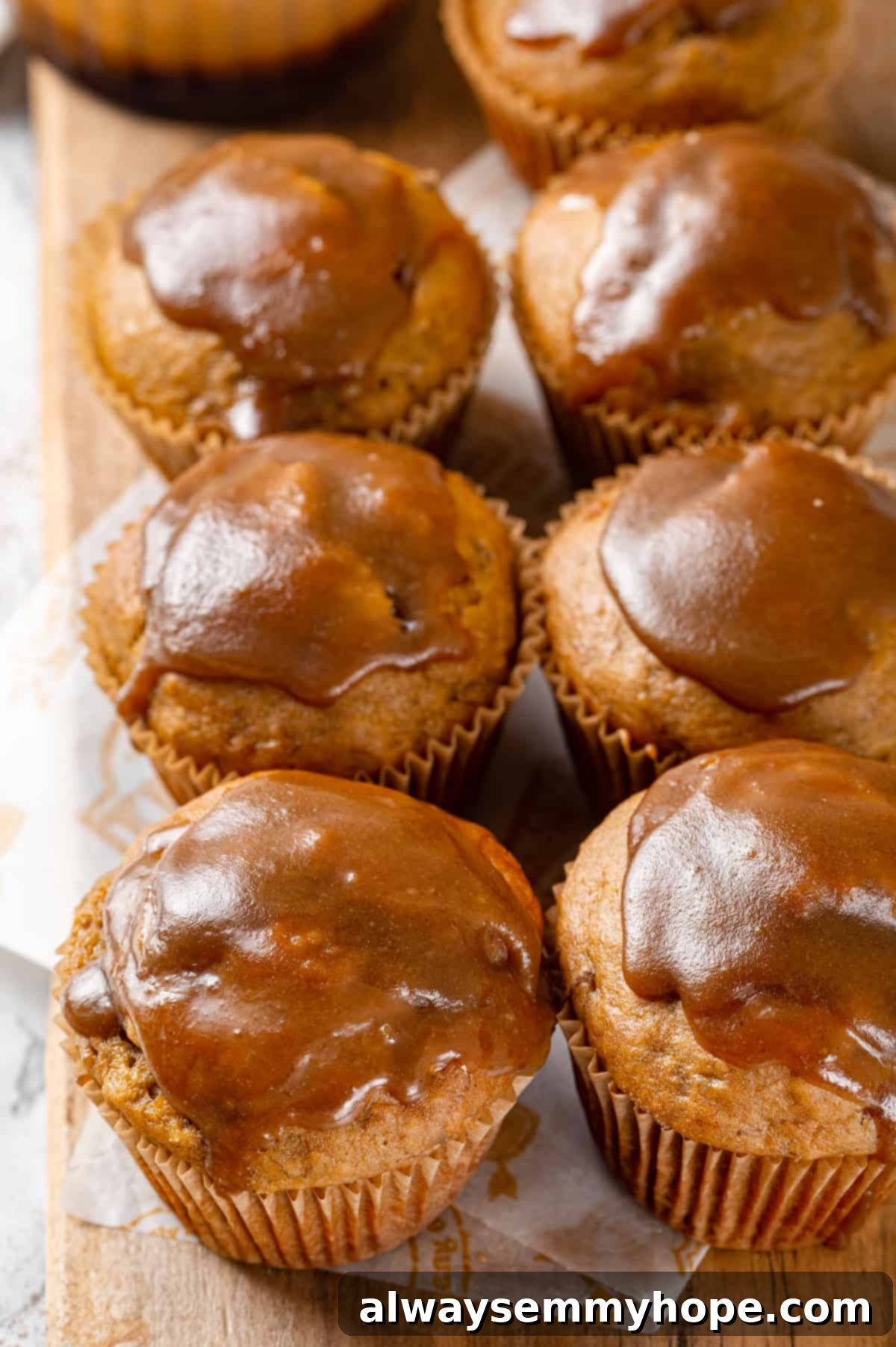 Glazed Pumpkin Banana Muffins Display Pumpkin banana muffins with a generous coating of glaze, neatly lined up on a rustic wooden board.