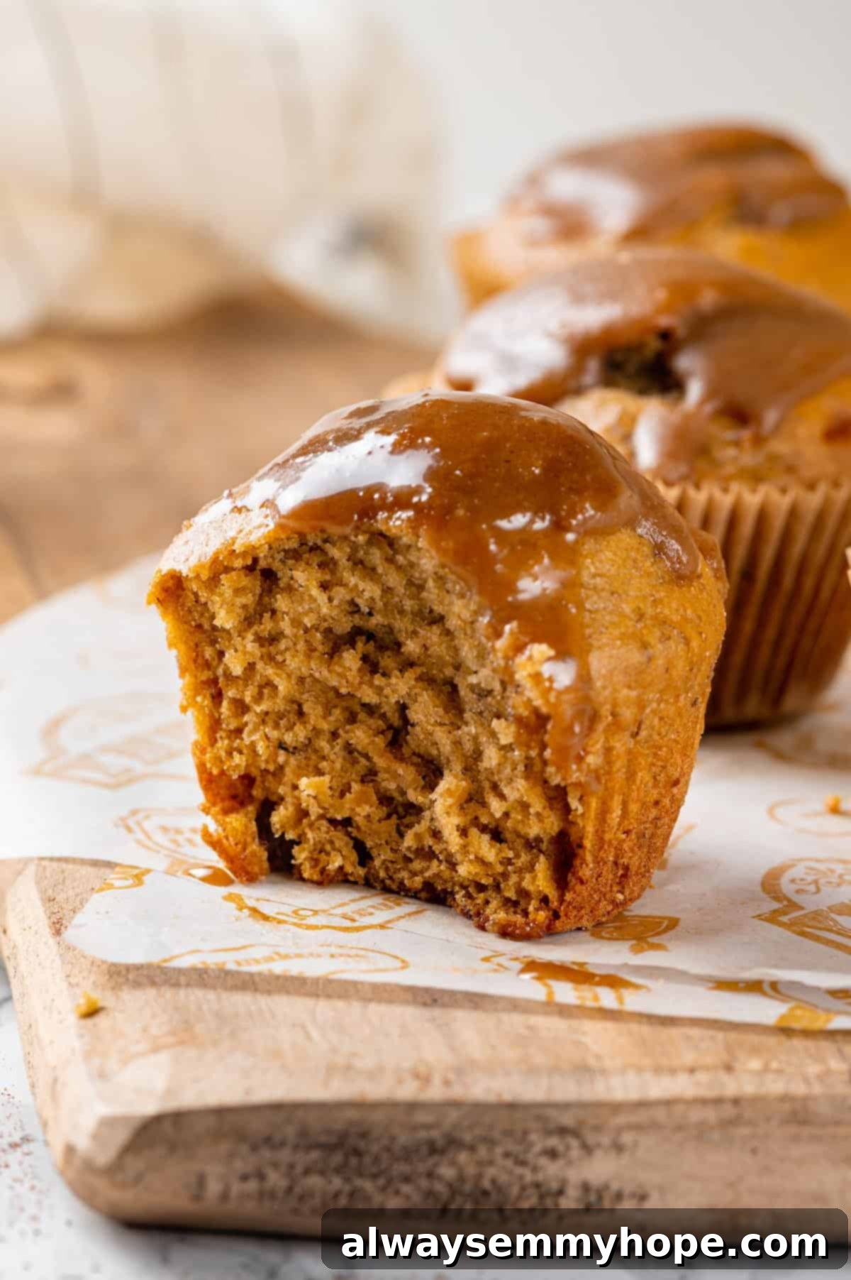 Inside a Glazed Pumpkin Banana Muffin A sliced pumpkin banana muffin on a wooden board, revealing its tender, moist interior, with two whole muffins in the background.