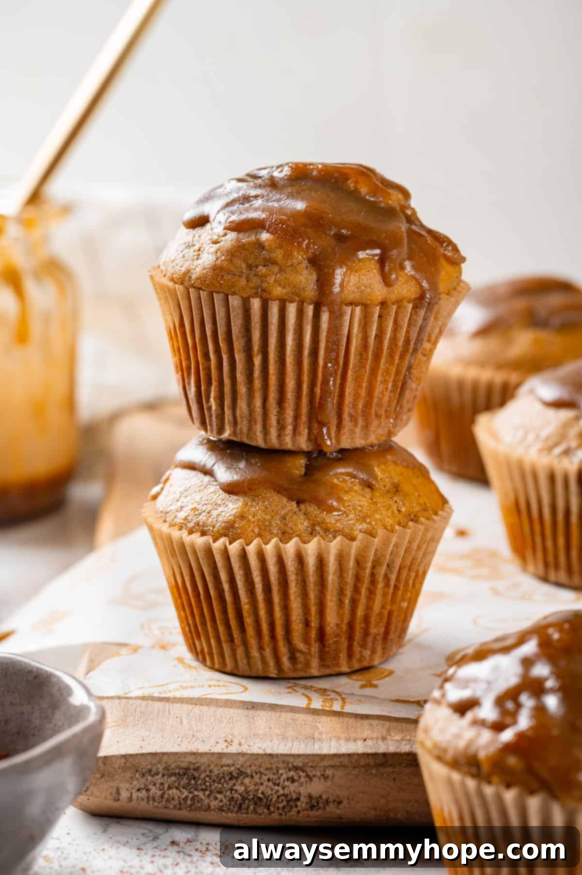 Stack of Glazed Pumpkin Banana Muffins Two glazed pumpkin banana muffins stacked on a wooden board, highlighting the glistening glaze.