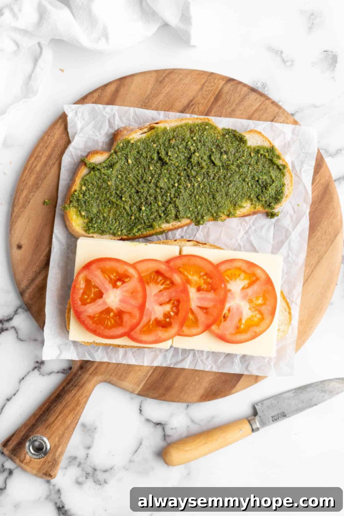 One slice of bread spread with pesto, another topped with mozzarella and tomatoes on round cutting board