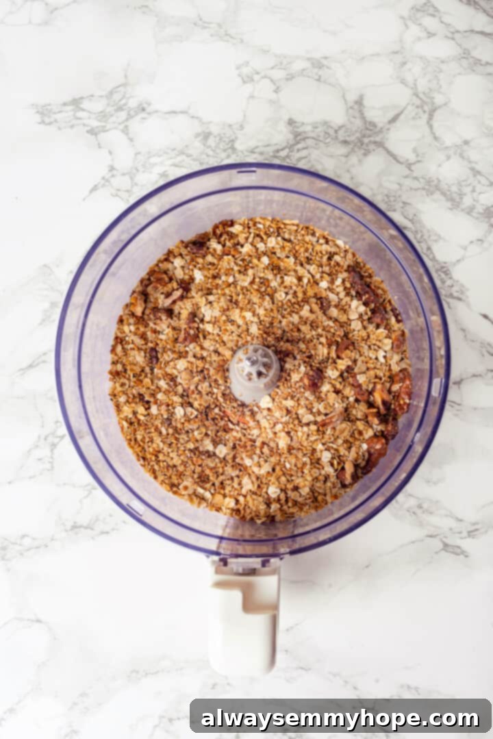 This easy homemade granola butter recipe is a toasty blend of oats, seeds, nuts and cozy spices. Spread it on toast, fruit, waffles and more! Overhead view of ingredients for granola butter in food processor before pulsing