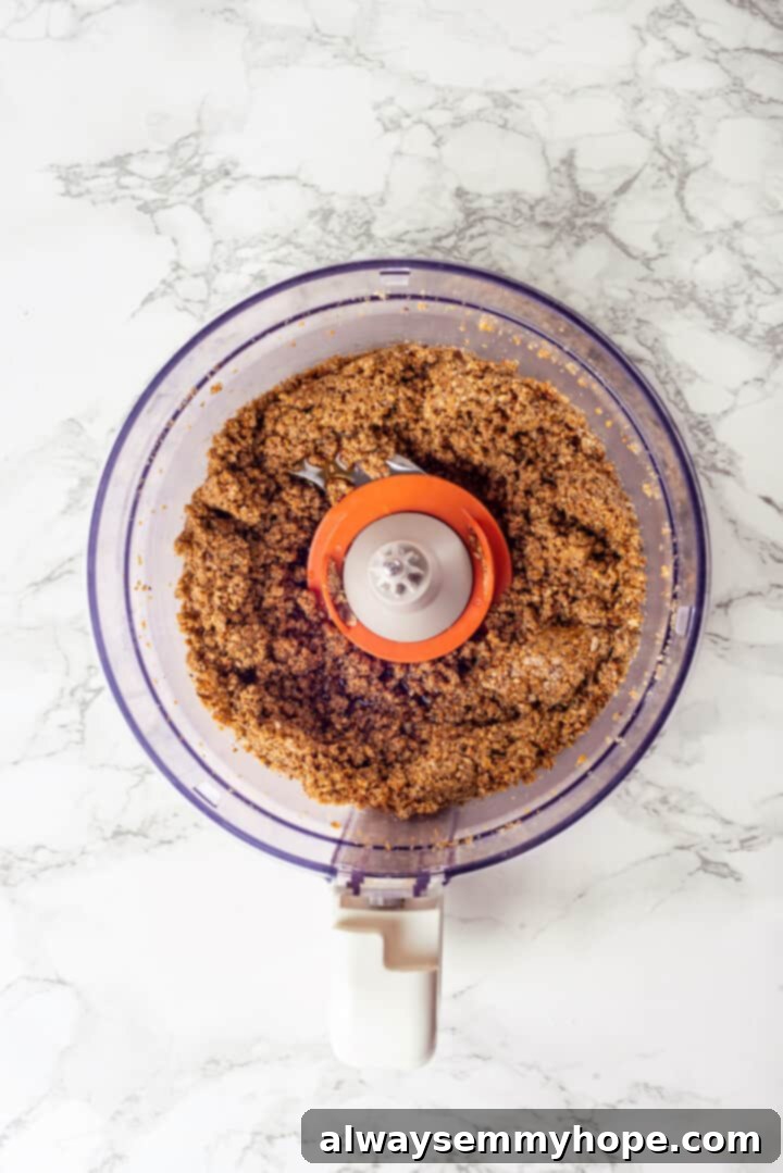 This easy homemade granola butter recipe is a toasty blend of oats, seeds, nuts and cozy spices. Spread it on toast, fruit, waffles and more! Overhead view of ingredients for granola butter in food processor after pulsing