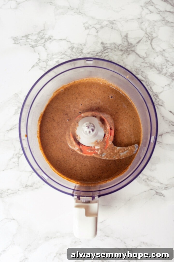 This easy homemade granola butter recipe is a toasty blend of oats, seeds, nuts and cozy spices. Spread it on toast, fruit, waffles and more! Overhead view of granola butter in food processor