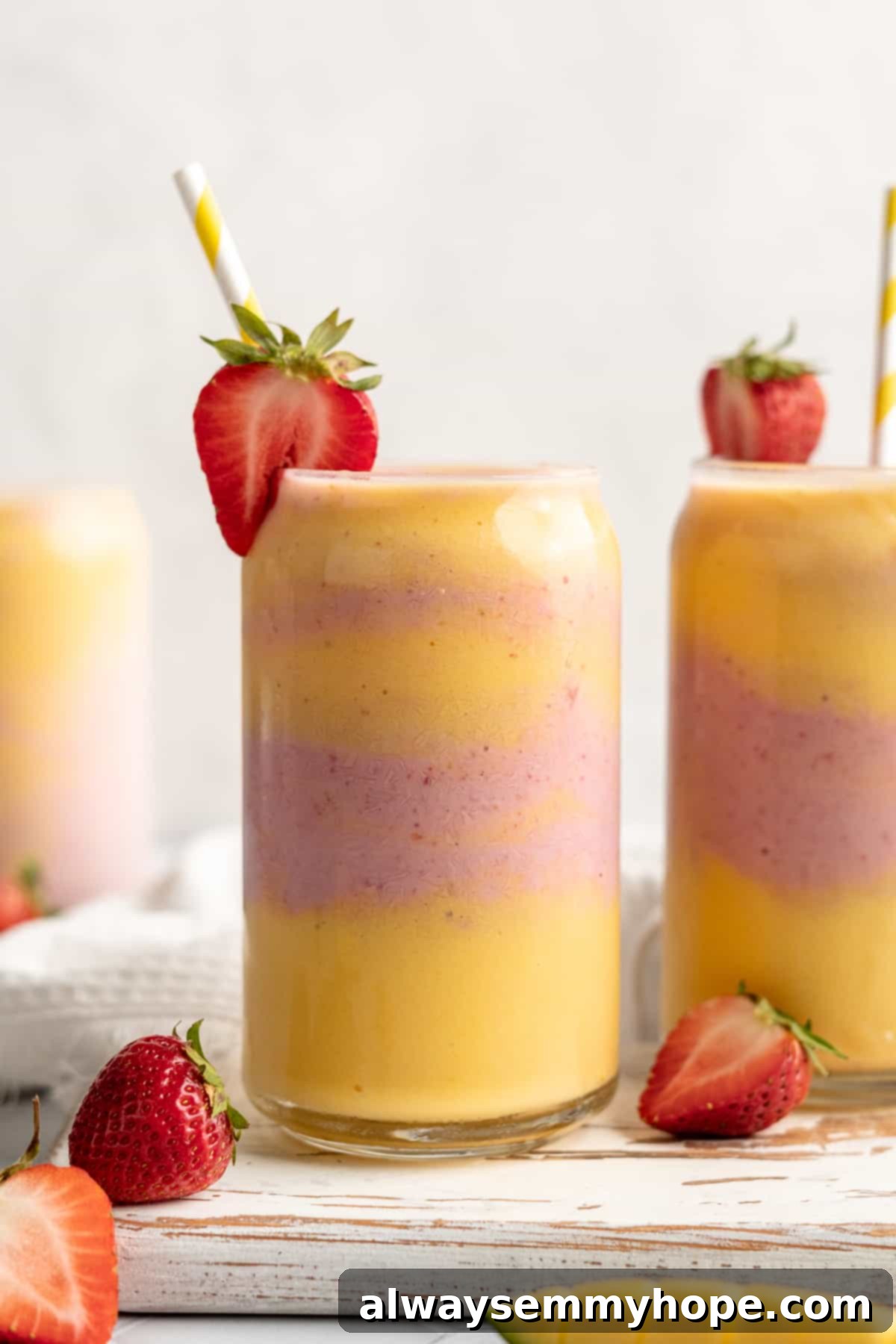 Two glasses of strawberry mango smoothie with straws and strawberries on rim