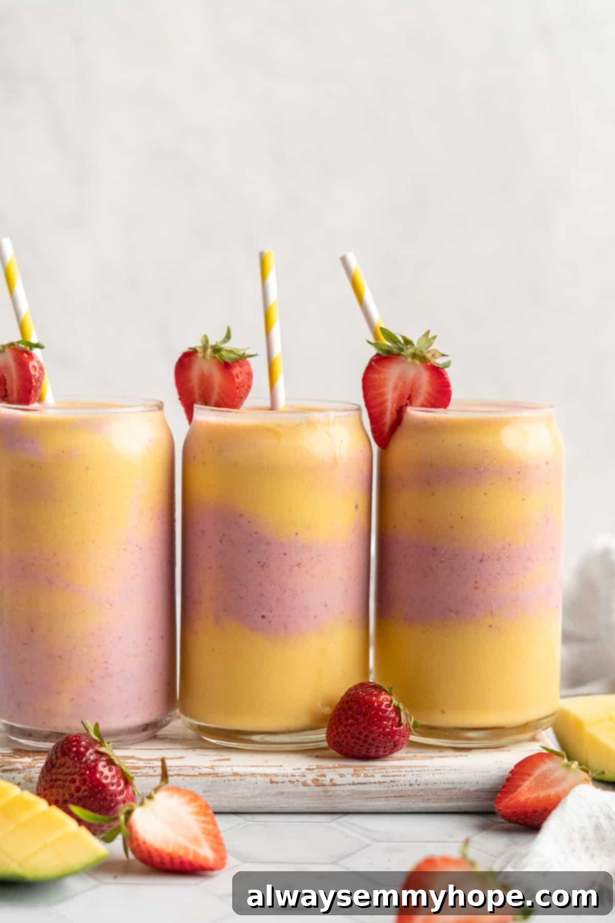 Three glasses of layered strawberry mango smoothie on a wooden board