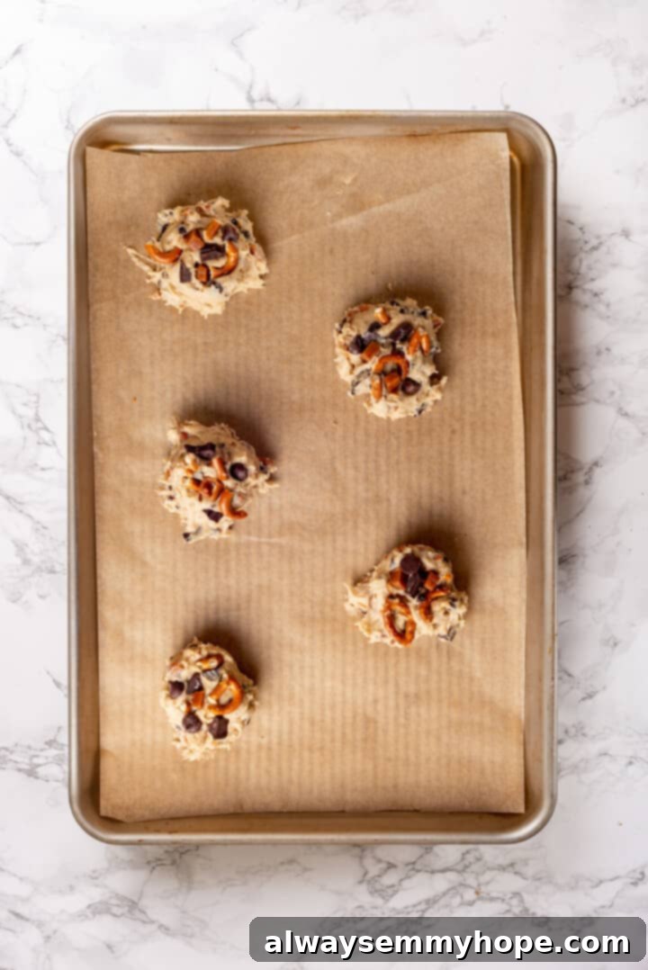 With an irresistible mix of chocolate, caramel and crispy pretzels, these kitchen sink cookies are easy to whip up and even easier to devour! Overhead view of vegan kitchen sink cookie dough balls, topped with extra mix-ins, arranged on a baking sheet before baking.