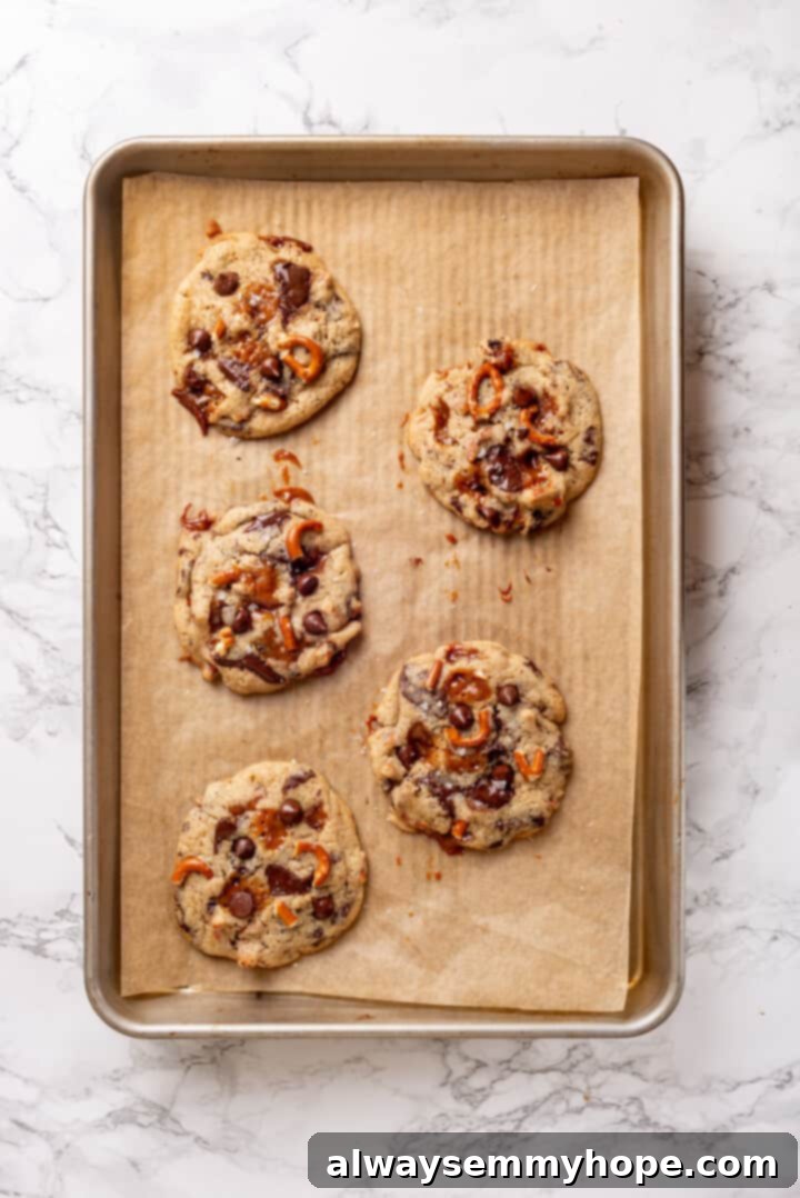 With an irresistible mix of chocolate, caramel and crispy pretzels, these kitchen sink cookies are easy to whip up and even easier to devour! Overhead view of freshly baked vegan kitchen sink cookies on a baking sheet, golden and slightly spread, ready for cooling.