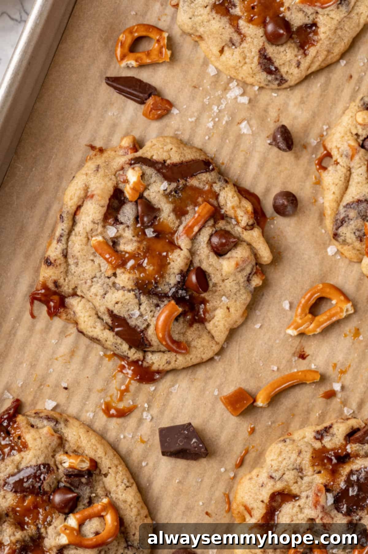 With an irresistible mix of chocolate, caramel and crispy pretzels, these kitchen sink cookies are easy to whip up and even easier to devour! Close-up of baked vegan kitchen sink cookies on a baking sheet, featuring visible pretzels, salt flakes, chocolate, and caramel pieces.