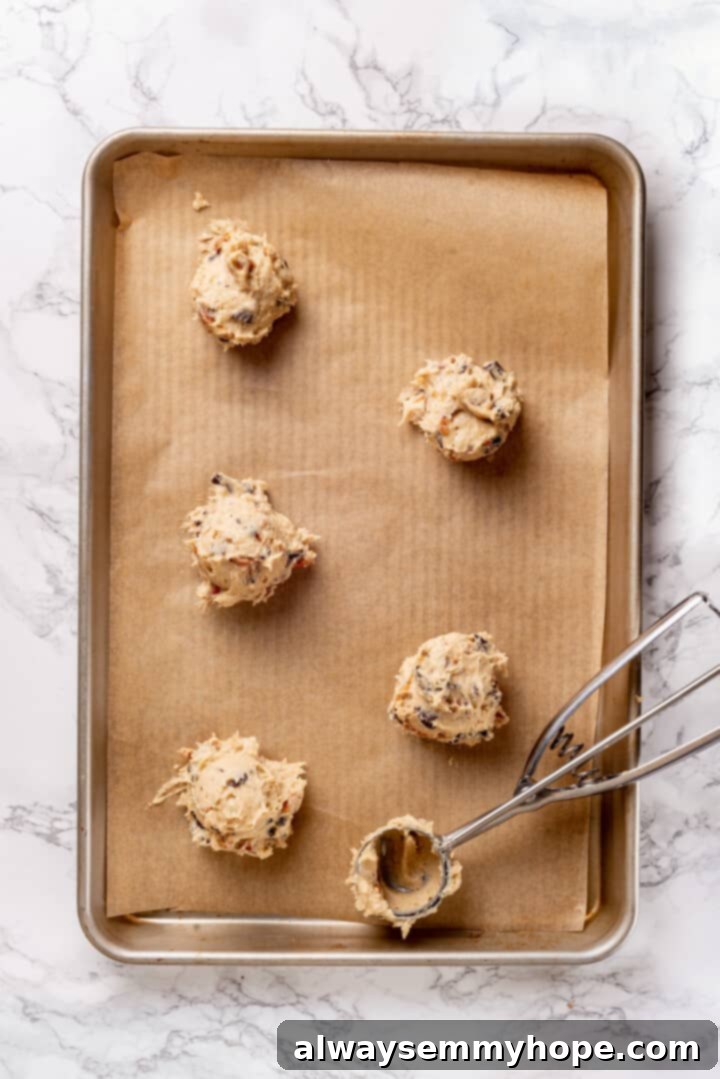 With an irresistible mix of chocolate, caramel and crispy pretzels, these kitchen sink cookies are easy to whip up and even easier to devour! Overhead view of scooped balls of vegan kitchen sink cookie dough placed on a parchment-lined baking sheet, ready for baking.