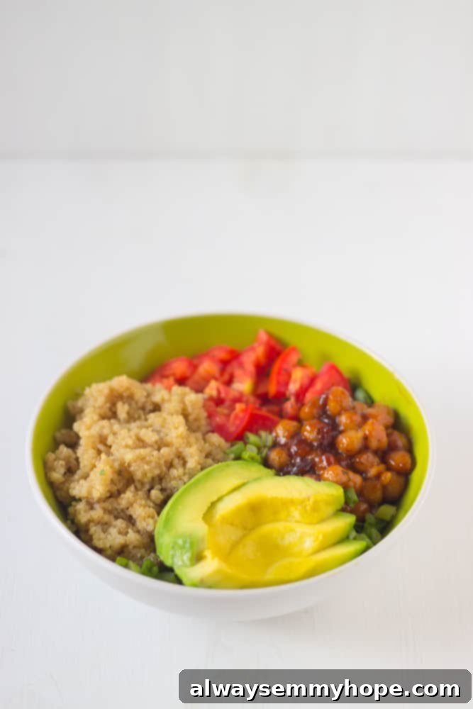 A close-up of the Tropical Quinoa Salad Bowl with BBQ Chickpeas, showcasing the fresh vegetables and flavorful ingredients for a wholesome meal! Side shot of veggie bowl with spicy chickpeas and avocado. The colorful ingredients are arranged artfully in the bowl.