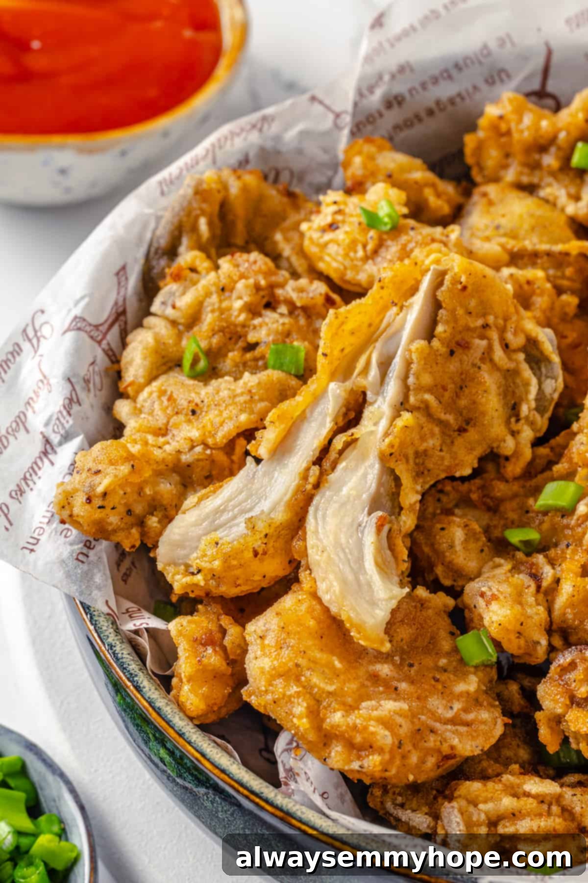 Experience the ultimate crispy and flavorful vegan fried chicken, featuring the incredible meaty texture of oyster mushrooms. A bowl of crispy vegan fried chicken made from oyster mushrooms, lined with parchment paper. One piece is cut open, revealing the mushroom's meaty texture.