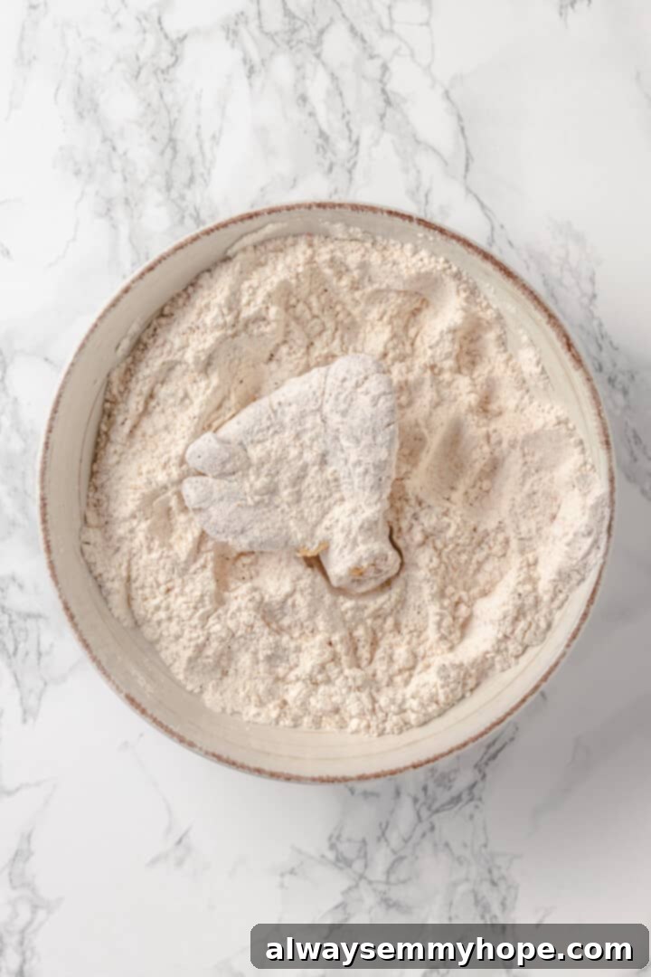 Ensuring a full, even coating for delicious vegan fried chicken. Overhead view of an oyster mushroom being carefully dredged in the seasoned flour mixture.