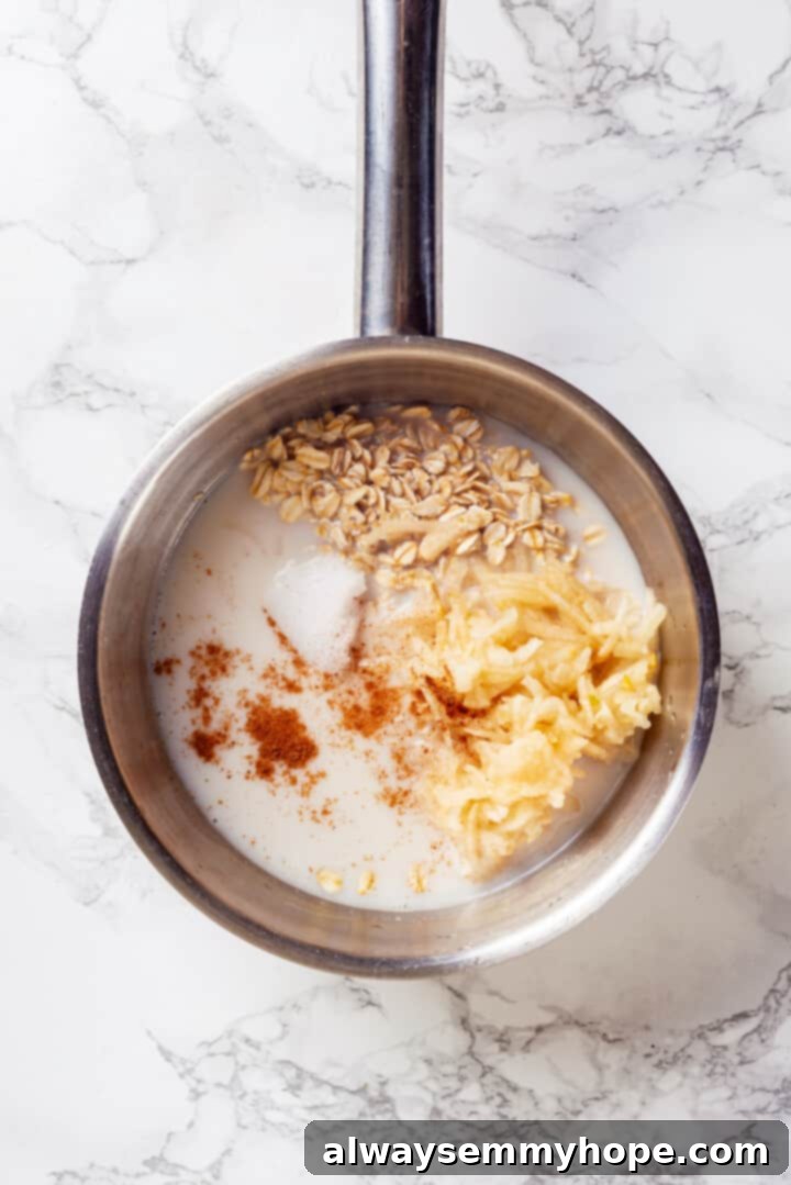 Overhead view of oats, water, cinnamon, pear, and coconut oil combined in a small saucepan.