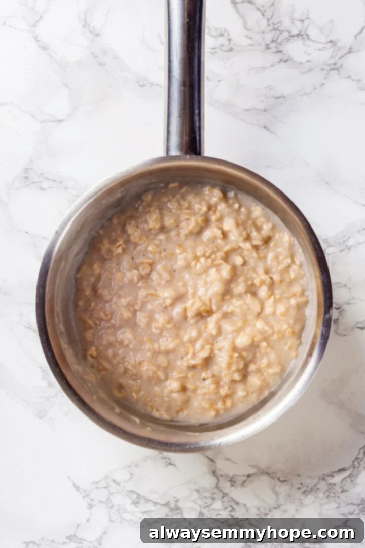 Overhead view of cooked baby oatmeal in a saucepan, showing its creamy texture.