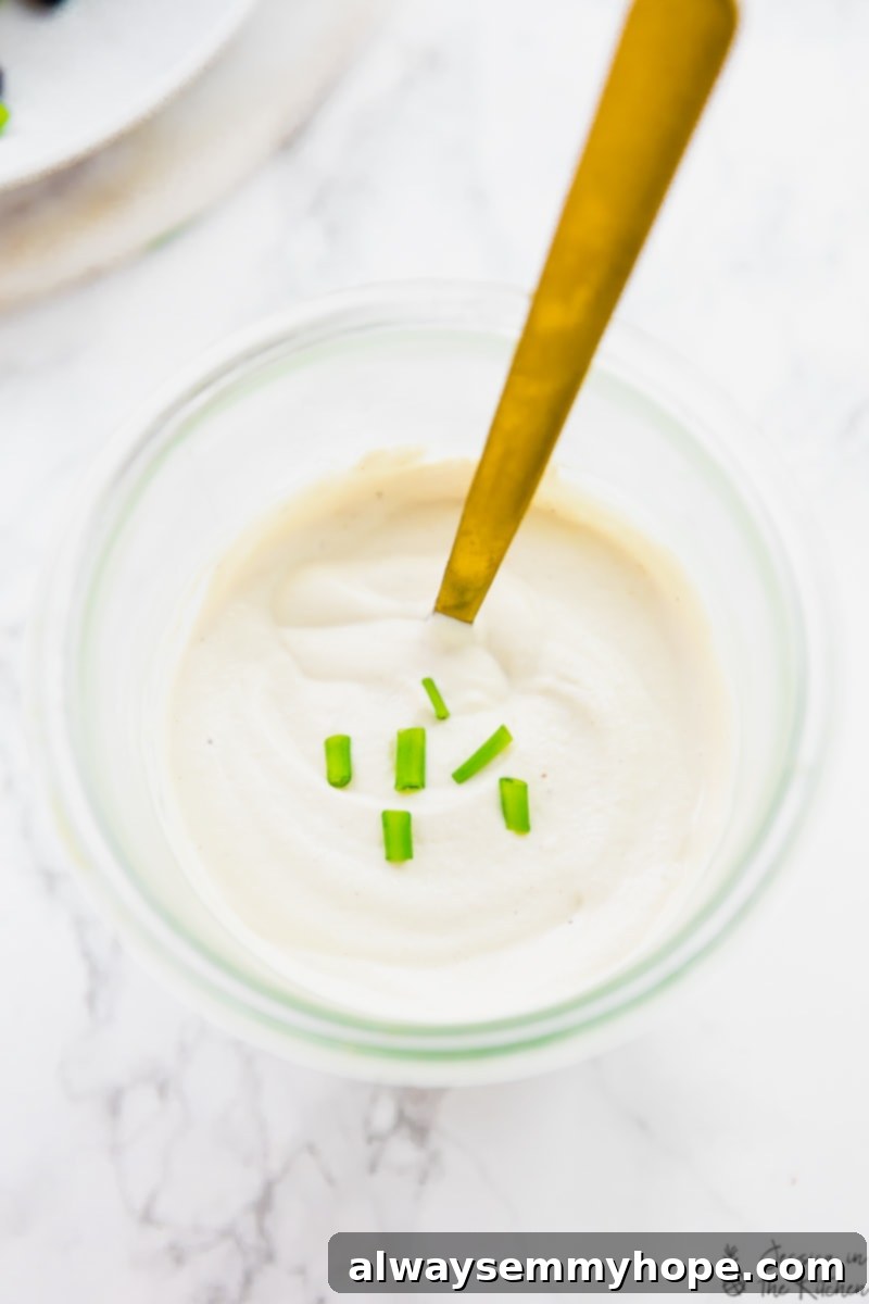 Jar of vegan sour cream with chives on top and spoon inside
