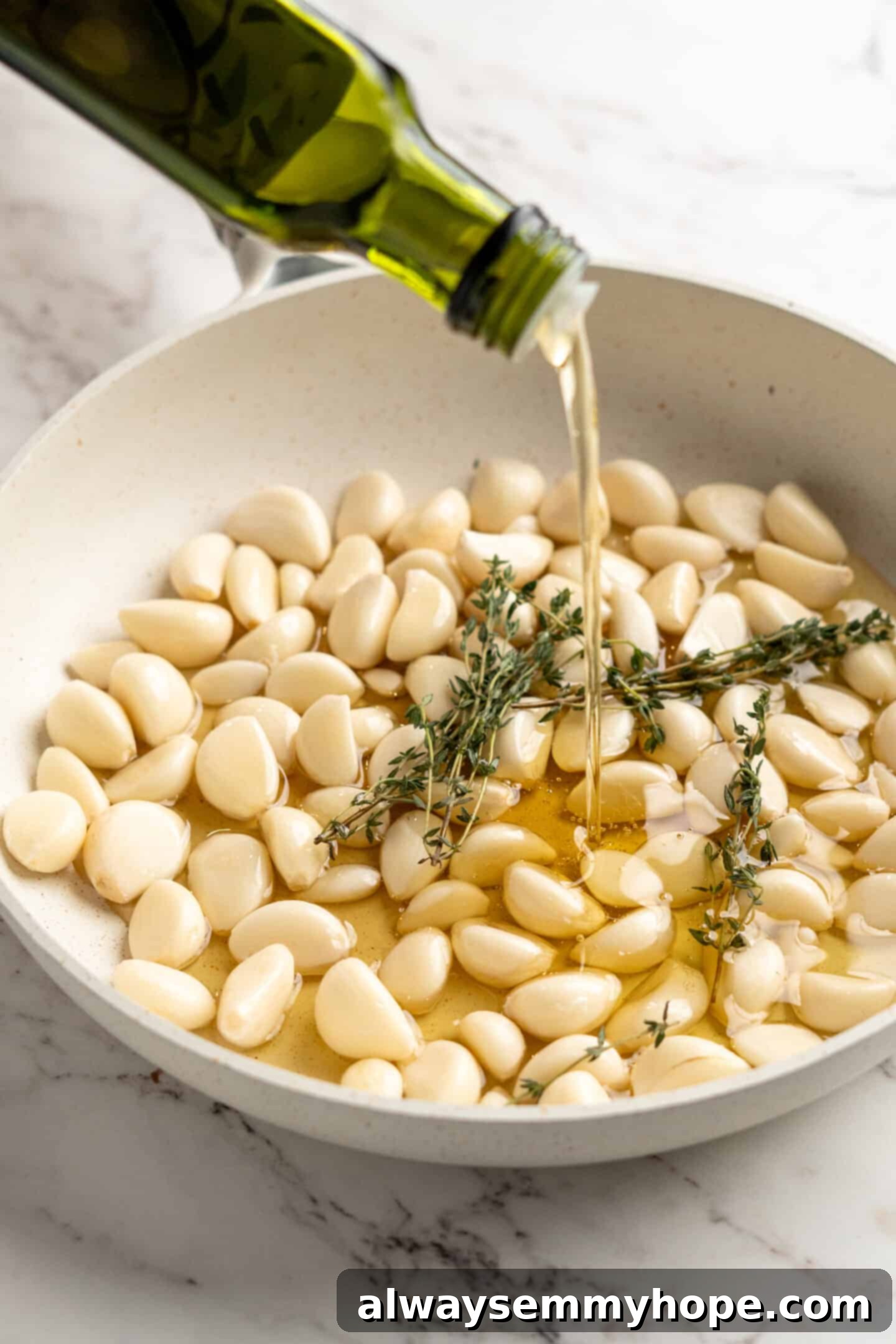 Pouring oil into pan with fresh thyme sprigs and peeled garlic cloves
