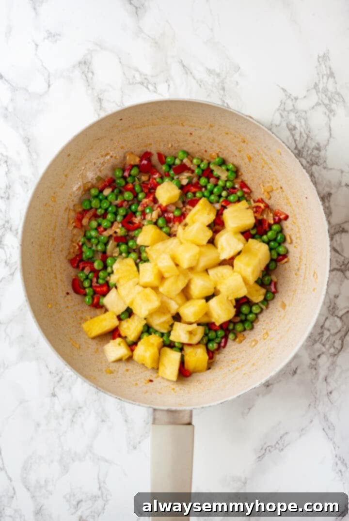 This easy homemade pineapple fried rice recipe gives you that perfect balance of sweet and salty flavour in every bite. Ready in minutes! Overhead view of pineapple added to pan with vegetables