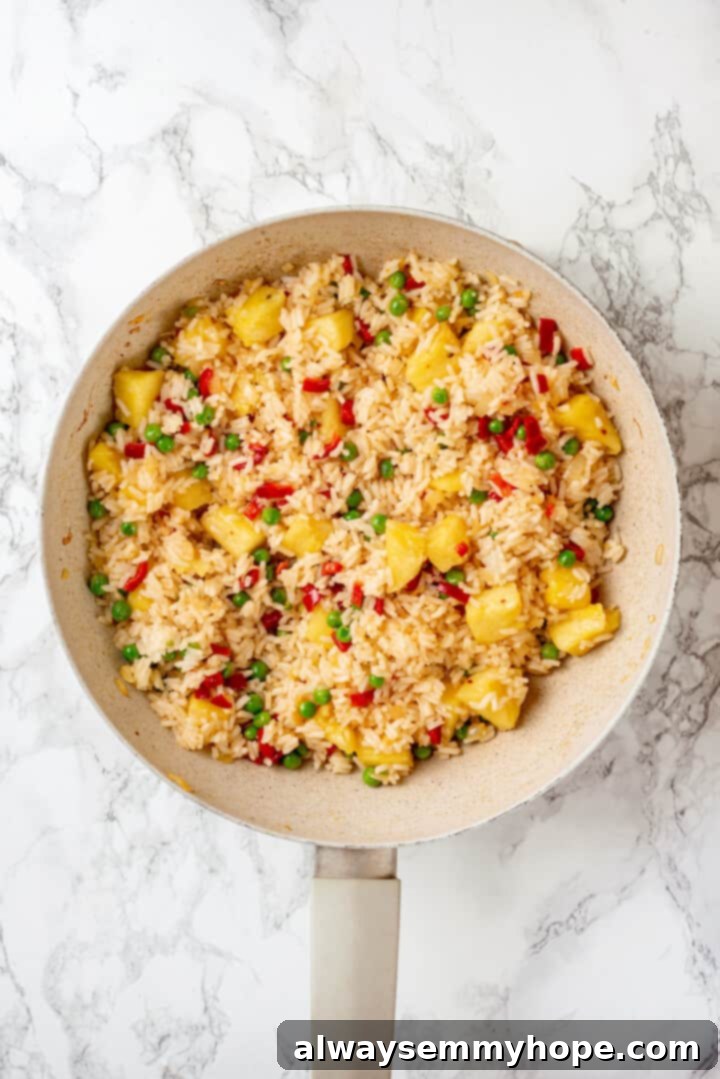This easy homemade pineapple fried rice recipe gives you that perfect balance of sweet and salty flavour in every bite. Ready in minutes! Overhead view of pineapple fried rice in pan before adding soy sauce