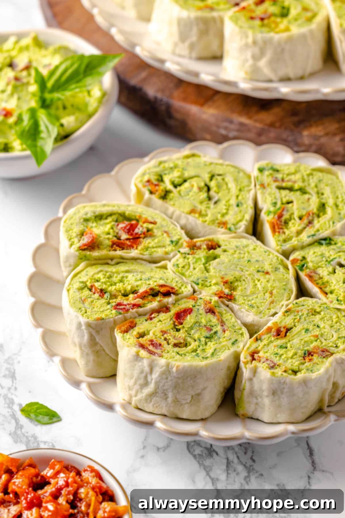 With cream cheese, pesto, Parmesan, and sun-dried tomatoes, these easy pinwheel sandwiches are full of flavour. Great for a party or lunch! Plate of pinwheel sandwiches with pesto
