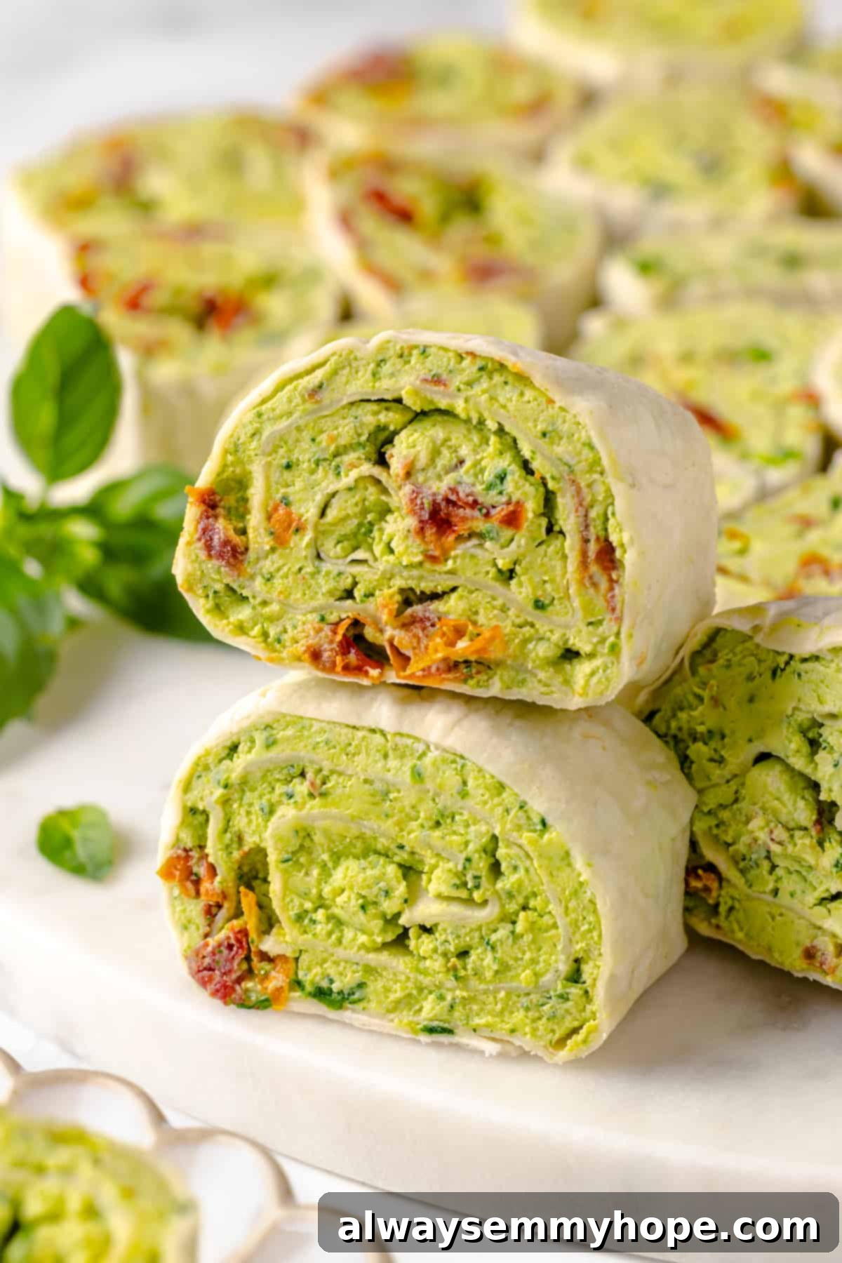 With cream cheese, pesto, Parmesan, and sun-dried tomatoes, these easy pinwheel sandwiches are full of flavour. Great for a party or lunch! Two pinwheel sandwiches stacked on top of each other