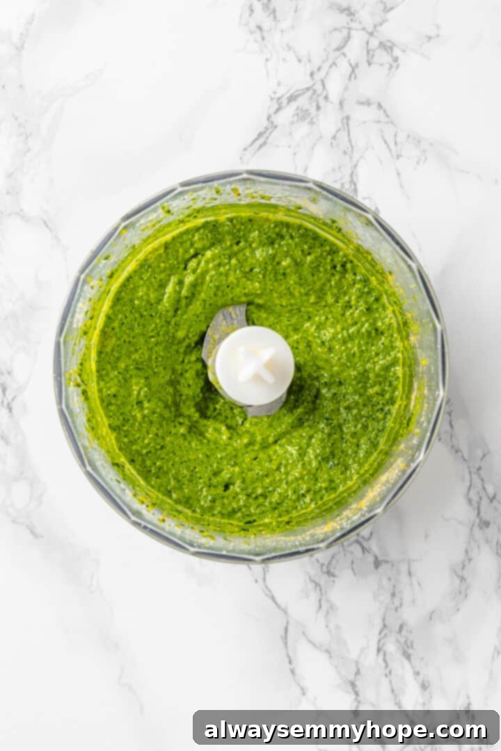 With cream cheese, pesto, Parmesan, and sun-dried tomatoes, these easy pinwheel sandwiches are full of flavour. Great for a party or lunch! Overhead view of pesto in food processor bowl