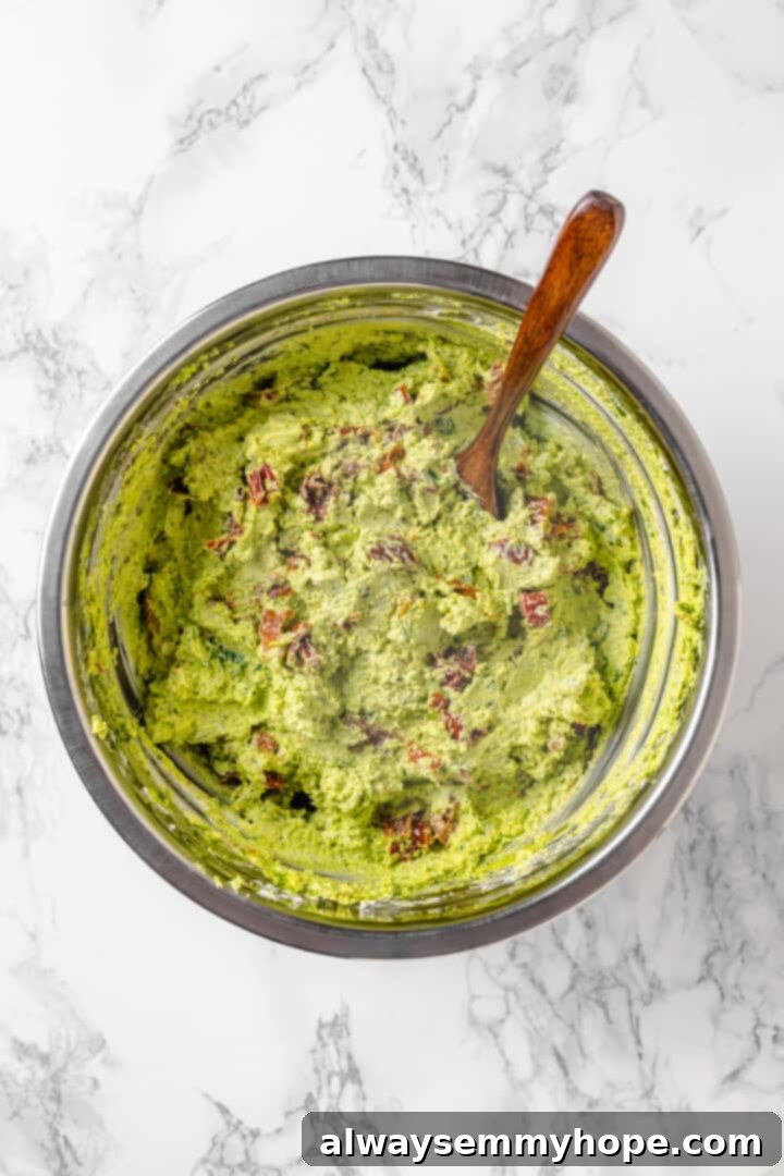 With cream cheese, pesto, Parmesan, and sun-dried tomatoes, these easy pinwheel sandwiches are full of flavour. Great for a party or lunch! Overhead view of pesto cream cheese mixture in bowl