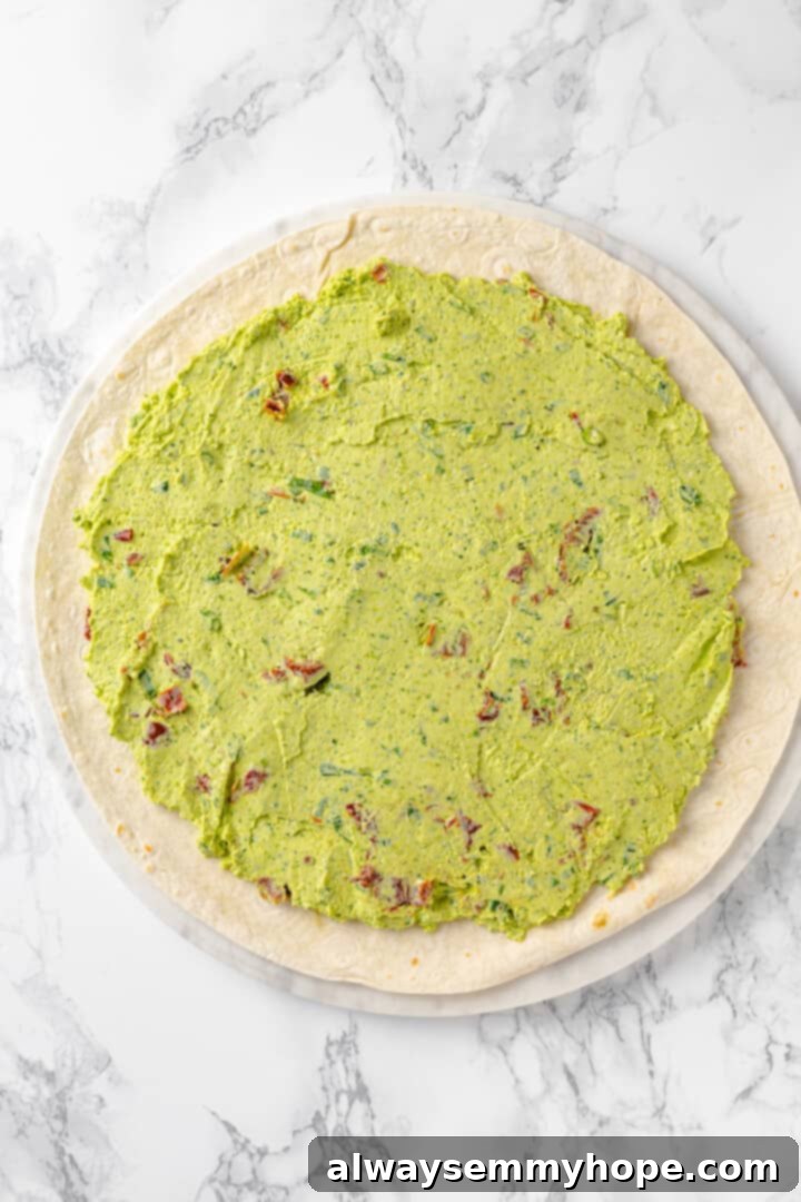 With cream cheese, pesto, Parmesan, and sun-dried tomatoes, these easy pinwheel sandwiches are full of flavour. Great for a party or lunch! Tortilla topped with pesto cream cheese