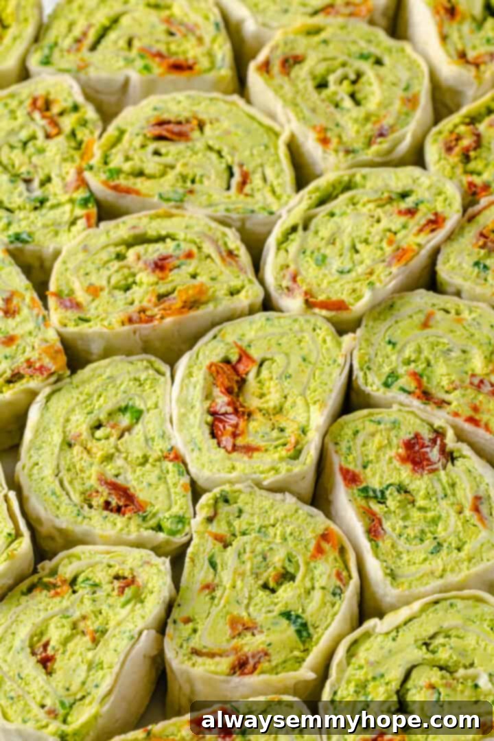 With cream cheese, pesto, Parmesan, and sun-dried tomatoes, these easy pinwheel sandwiches are full of flavour. Great for a party or lunch! Overhead view of pesto roll-ups tightly packed together on platter