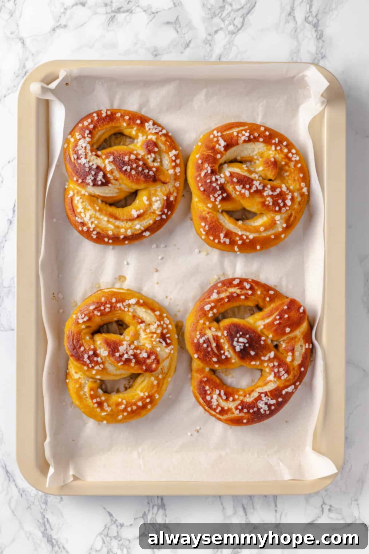 This soft pretzel recipe is fun to make and the results are outstanding—chewy, buttery, and perfect to serve with your fave dipping sauce! Overhead view of 4 vegan pretzels on sheet pan