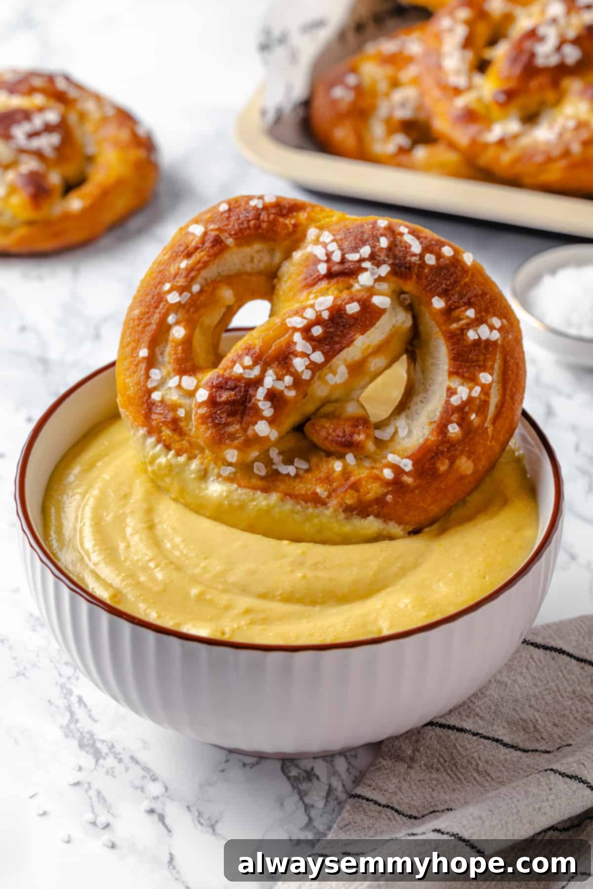 This soft pretzel recipe is fun to make and the results are outstanding—chewy, buttery, and perfect to serve with your fave dipping sauce! Vegan soft pretzel being dipped into beer cheese