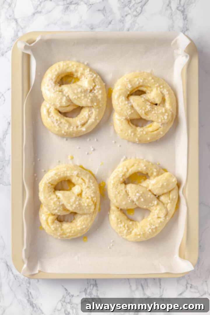 This soft pretzel recipe is fun to make and the results are outstanding—chewy, buttery, and perfect to serve with your fave dipping sauce! Overhead view of unbaked soft pretzels on sheet pan after adding salt