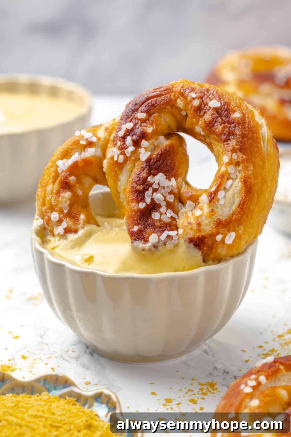 Soft pretzel being dipped into a bowl of creamy vegan pretzel dip, glistening with cheese sauce