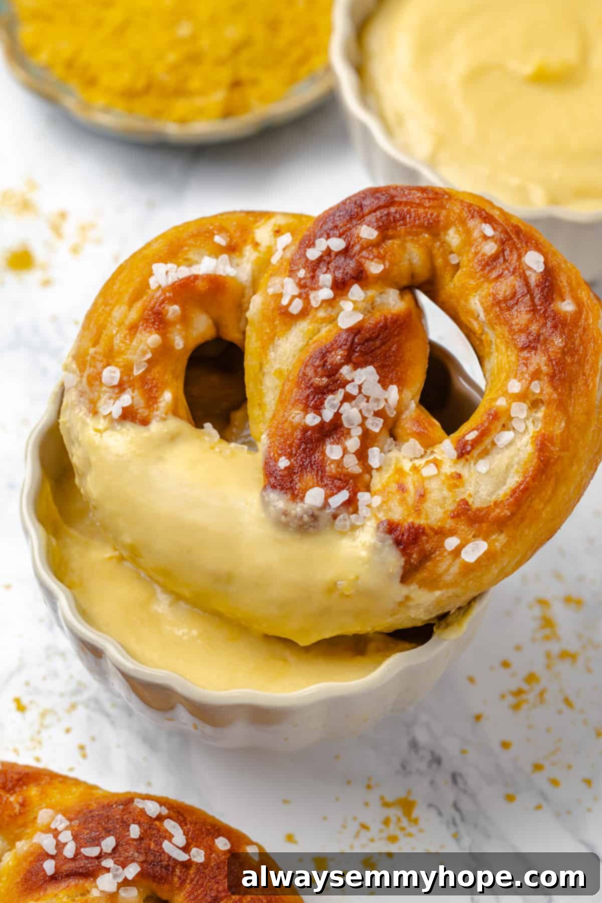 Soft pretzel being dipped into a bowl of golden, cheesy vegan pretzel dip